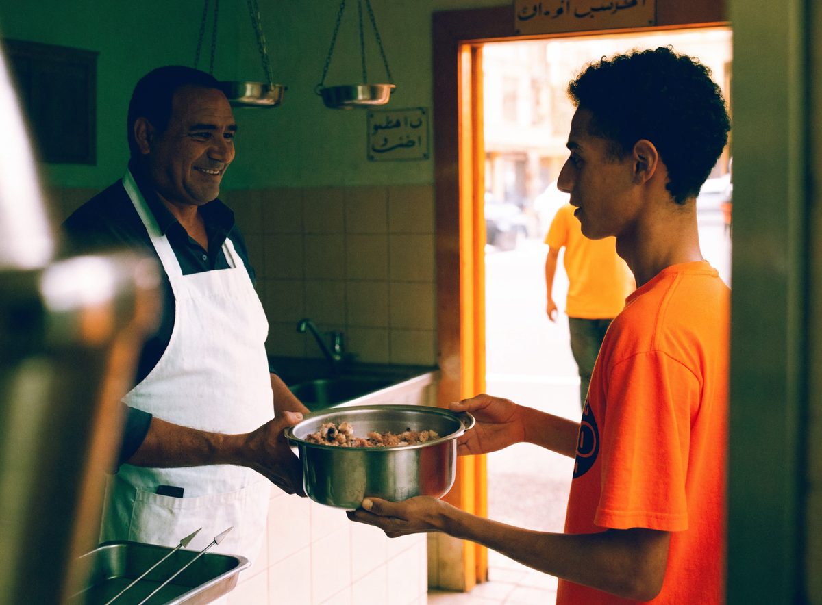 A butcher handing a sealed container of trimmings to a volunteer